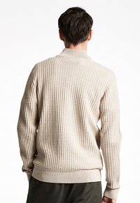 Maglione beige con texture e colletto polo, caratterizzato da un motivo a maglia e polsini a coste, mostrato da dietro.