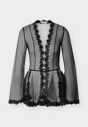 Blouse noire en voile transparent à manches longues avec bordure en dentelle florale sur le devant, les poignets et l'ourlet, présentant un décolleté en V profond et une taille cintrée.