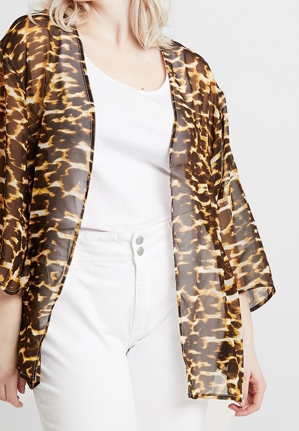 Transparante bruine kimono met luipaardprint, open voorkant en brede mouwen, gedragen over een wit shirt en gecombineerd met een witte broek.
