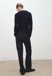Suéter de punto acanalado en azul marino oscuro con cuello redondo, combinado con pantalones a rayas finas en gris carbón. Textura de tela suave y silueta ajustada.