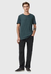 Turkos crew-neck t-shirt med korta ärmar, kombinerad med svarta jeans och grå sneakers. Enkel design, mjuk textur, inga synliga mönster.