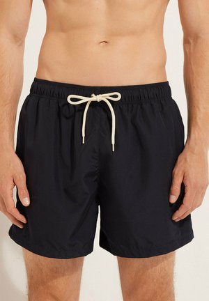 Marineblaue Schwimmshorts aus leichtem Stoff, ausgestattet mit einem elastischen Bund mit einer cremefarbenen Kordel und seitlichen Nahttaschen.