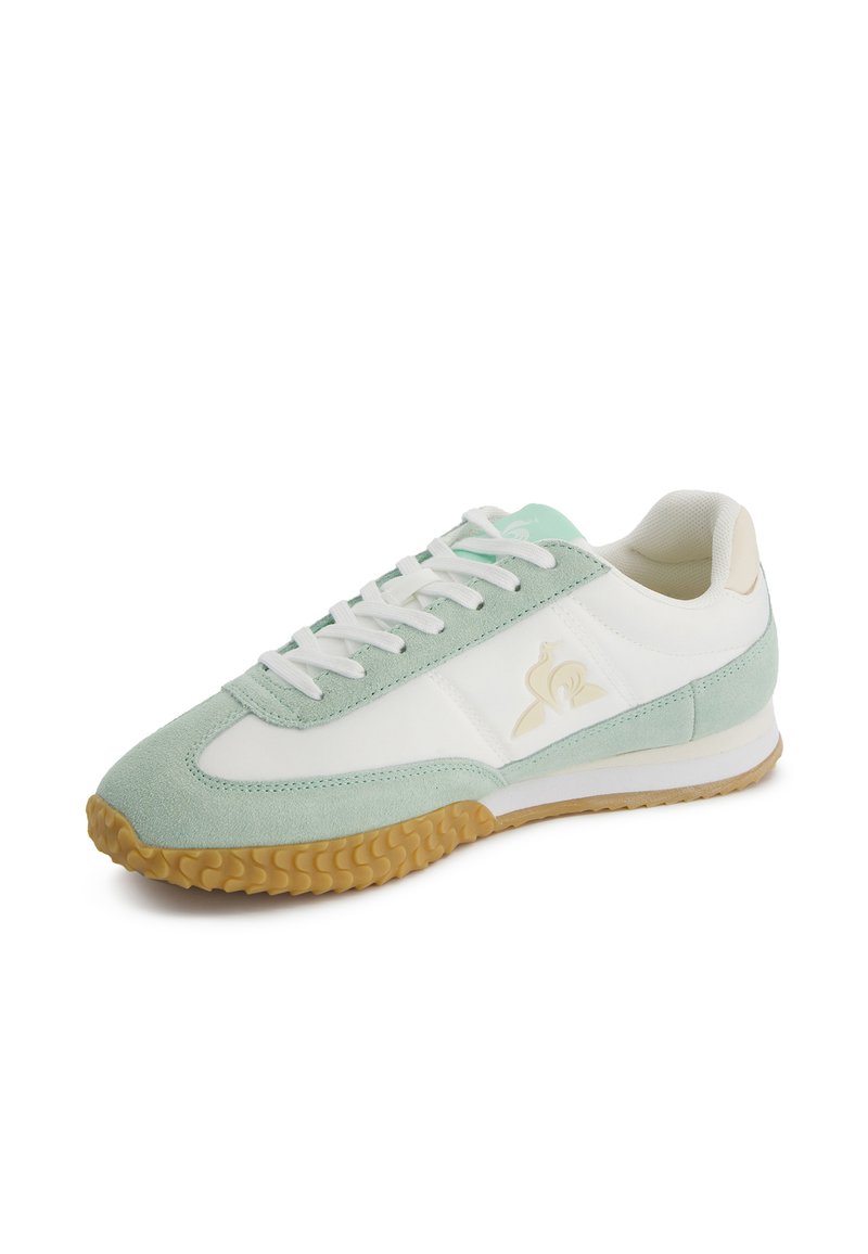 Zapatilla deportiva en verde claro y blanco, con parte superior de ante, suela de goma y acentos beige en contraste; incluye cordones planos y logotipo.