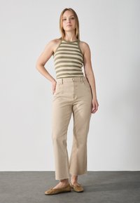 Beige avkortade jeans med fransiga fållar, ihop med en grön och beige randig linne. Modellen står med en hand på höften och bär bruna ballerina skor.