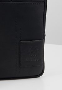 Borsetta in pelle nera con una superficie testurizzata, caratterizzata da cuciture sottili e un logo del marchio impresso su una toppa rettangolare.