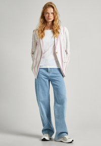 Prugasta blazer v beli, roza in zeleni barvi s posameznim gumbom, kombinirana z belo srajco in svetlo modrimi širokimi jeans hlačami.