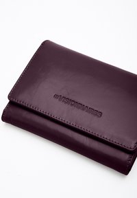 Violet leather wallet with embossed "LES VISIONNAIRES" logo, textured surface, and stitched edges, featuring a rectangular folded design.