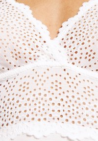 White lace top featuring a V-neck design, intricate open patterns, scalloped edges, and a textured finish across the bodice.