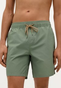 Shorts de bain verts avec une taille élastique et un cordon de serrage beige, présentant une texture lisse et un design simple.