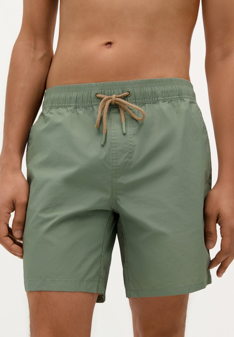 Shorts de bain verts avec une taille élastique et un cordon de serrage beige, présentant une texture lisse et un design simple.