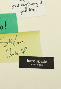 Vit bakgrund med färgglada klisterlappar i grönt och gult, med handskriven text och en svart etikett som står "kate spade NEW YORK."