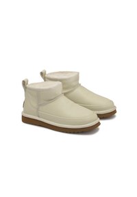 Botines de cuero crema con un suave forro de piel texturizada, suela de goma plana y tiradores en la parte posterior para facilitar su uso.