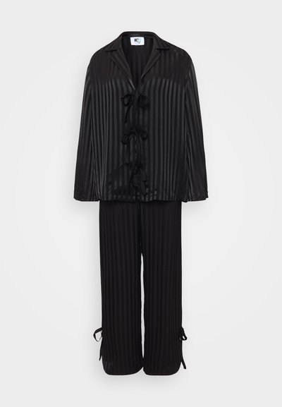 Conjunto de loungewear de satén negro que incluye una camisa de botones con acentos de lazo y pantalones a juego con dobladillos atados. Las rayas verticales realzan la textura.
