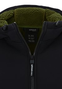 Schwarze Softshelljacke mit einer grün gefütterten Kapuze, durchgehendem Reißverschluss und einem Etikett mit Pflegehinweisen und Produktdetails.