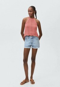 Rosa stickad halterneck-top med mönster i öppet arbete, kombinerad med ljusblå denim-shorts och bruna flip-flops. Enkla och avslappnade sommarkläder.