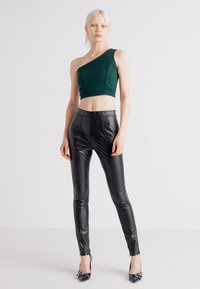 Zeleni crop top s jednim ramenom uparen s crnim kožnim tajicama visokog struka, s glatkom teksturom i prilagođenim dizajnom.