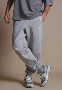 Pantaloni sportivi grigi con polsini a costine, caratterizzati da un piccolo logo di un elefante giallo. Indossati con scarpe da ginnastica grigie e bianche. Design a vestibilità rilassata.