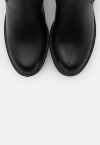 Botines negros hasta el tobillo con acabado en cuero sintético liso, punta redondeada, suela texturizada y detalle sutil de costura a lo largo del borde.