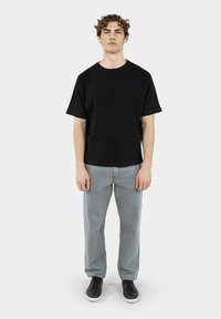 Svart kortermet skjorte med ribbestruktur, kombinert med lysegrå denimjeans og svarte sneakers. Enkel, avslappet passform og minimalistisk design.