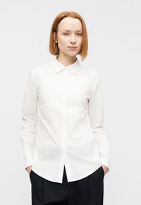 Λευκό πουκάμισο με κουμπιά, κλασικό γιακά, μακριά μανίκια και ίσια γραμμή. Κατασκευασμένο από απαλό ύφασμα με καθαρό, μίνιμαλ σχέδιο.