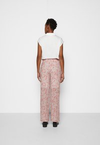 Top branco de manga curta combinado com calças de cintura alta e pernas largas, apresentando um padrão floral em rosa e vermelho sobre um fundo claro. Calçado preto.