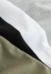 Baumwollstoffabschnitte in Grau, Weiß, Schwarz und Olivgrün, mit sichtbaren Nähten und glatter Textur. Klare geometrische Formen.