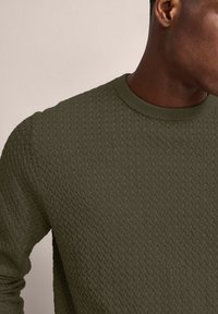 Maglione lavorato a maglia di colore verde oliva con un motivo testurizzato, colletto a costine e maniche terminate a polsino. Focalizzarsi sui dettagli del materiale e del design.