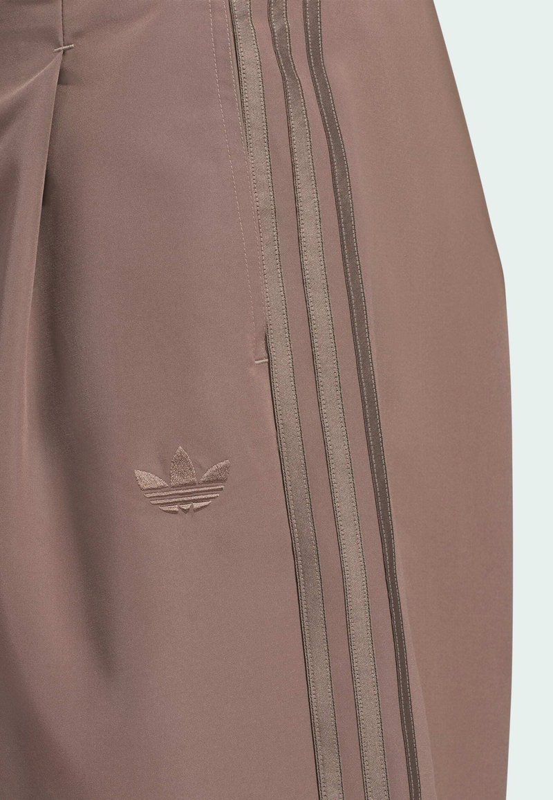 Brown fabric pants with three vertical darker brown stripes and a small embroidered adidas trefoil logo near the pocket.