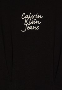Črna majica s kratkimi rokavi z belim izvezenim logotipom "Calvin Klein Jeans". Tkanina je gladka s rahlim raztegom in ima obliko kroga pri vratu.