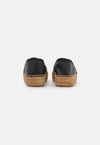 Black slip-on espadrilles with a woven jute sole. Smooth leather upper, rounded shape, elastic at the opening, and textured sole.