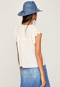 Witte blouse met geschulpte kant mouwen, zachte stof, losse pasvorm, gecombineerd met een blauwe geweven strohoed met een gevlochten accent.