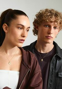 Collar con un colgante de oro; modelo vistiendo una sudadera color burdeos. Chaqueta de cuero texturizada en un modelo masculino; ambos llevan prendas neutras.