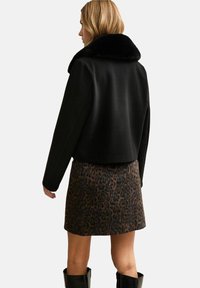 Czarny krótki płaszcz z teksturowanym czarnym sztucznym kołnierzem z futra, zestawiony z spódnicą w panterkę. Strój ma długie rękawy i dopasowany krój.