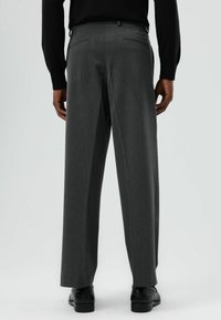 Grijze, op maat gemaakte broek met rechte pijpen, voorzien van twee achterzakken en een gladde textuur. Draagt bij een zwarte longsleeve.