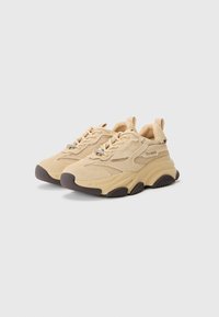 Zapatillas beige que combinan materiales de ante y malla, con puntera redonda, suela de goma gruesa y costuras detalladas, además de una lengüeta en el talón.