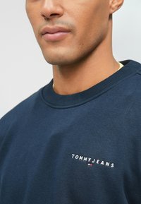 Sweatshirt azul-marinho com gola redonda, punhos canelados e logótipo bordado "TOMMYJEANS" em branco com um acento em vermelho e azul.