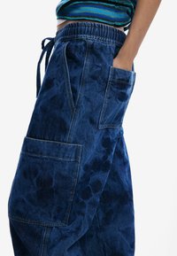 Pantalon cargo en denim bleu foncé avec une finition texturée, doté d'une taille élastique, d'un cordon de serrage et de grandes poches latérales.