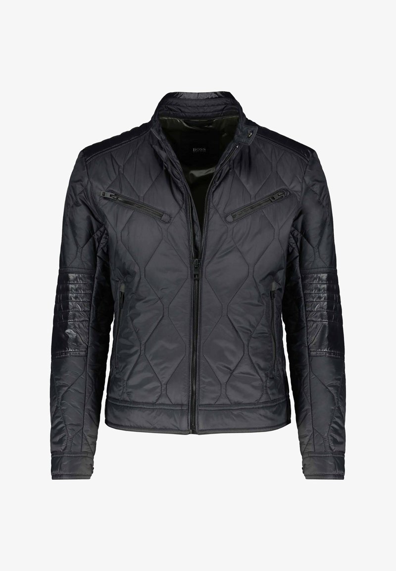 Mustat vuoratut takit, jossa on pystykaulus, vetoketjulliset taskut sekä teksturoidut olka- ja hiho-paneelit. Valmistettu kevyestä, kiiltävästä kankaasta.