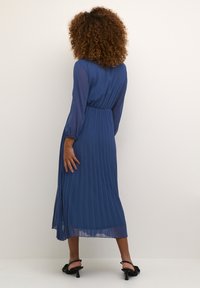 Blue pleated maxi dress with long sheer sleeves and a cinched waist. Features a flowy silhouette and semi-translucent fabric.
