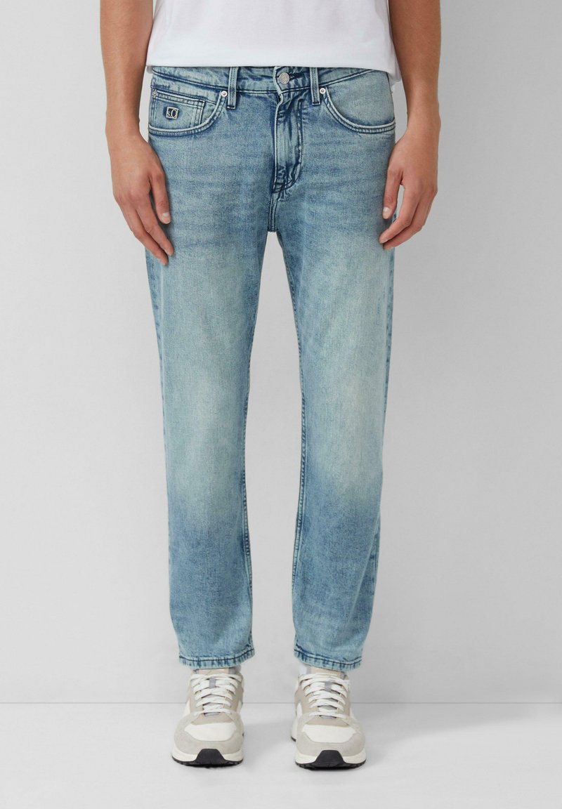 Hellblaue Denim-Jeans mit geradem Schnitt, im Fünf-Taschen-Stil, mit Knopfverschluss und subtilen Verwaschungen, kombiniert mit beigen Sneakers.