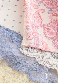 Prim-plan cu țesătură ce arată margini din dantelă moale în albastru, crem și alb, cu modele paisley roz și cu buline albastre pe fundaluri deschise.