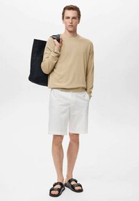 Beige long-sleeve top, white shorts, and black sandals. The individual carries a black tote bag, highlighting a casual outfit.