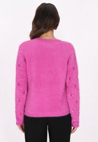 Flauschiger pinker Pullover mit langen Ärmeln, der Paillettenakzente an den Ärmeln, einen runden Ausschnitt und eine weiche Textur aufweist.