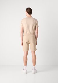 Beige rövidnadrág és hozzáillő póló sima anyagból, amely laza fazonú, rugalmas derékrésszel rendelkezik, és a rövidnadrág hátulján egy zseb található.