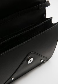 Borsa a tracolla in pelle nera con hardware argentato, caratterizzata da un flap triangolare, ampi scomparti interni e una superficie liscia.