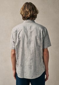 Kurzärmliges, hellgraues Hemd mit dezentem Blumenmuster, Kentkragen und abgerundetem Saum, aus einem strukturierten, leichten Stoff gefertigt.