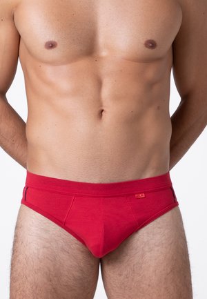 Slip di cotone rosso con dettagli laterali a contrasto, caratterizzati da un'ampia vita e una texture liscia. Il design è aderente, enfatizzando la forma.