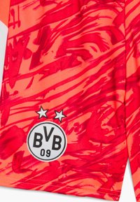 Maillot de sport orange vif avec des motifs abstraits rouges. Il présente un logo circulaire avec "BVB 09" et deux étoiles au-dessus, fabriqué en tissu léger.