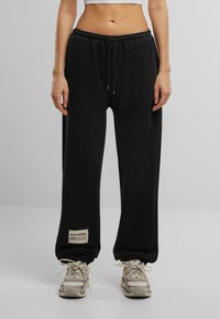 Schwarze Jogginghosen aus weichem Material, mit einem Kordelzug am Bund, elastischen Bündchen und einem kleinen Etikett mit Text am linken Bein.