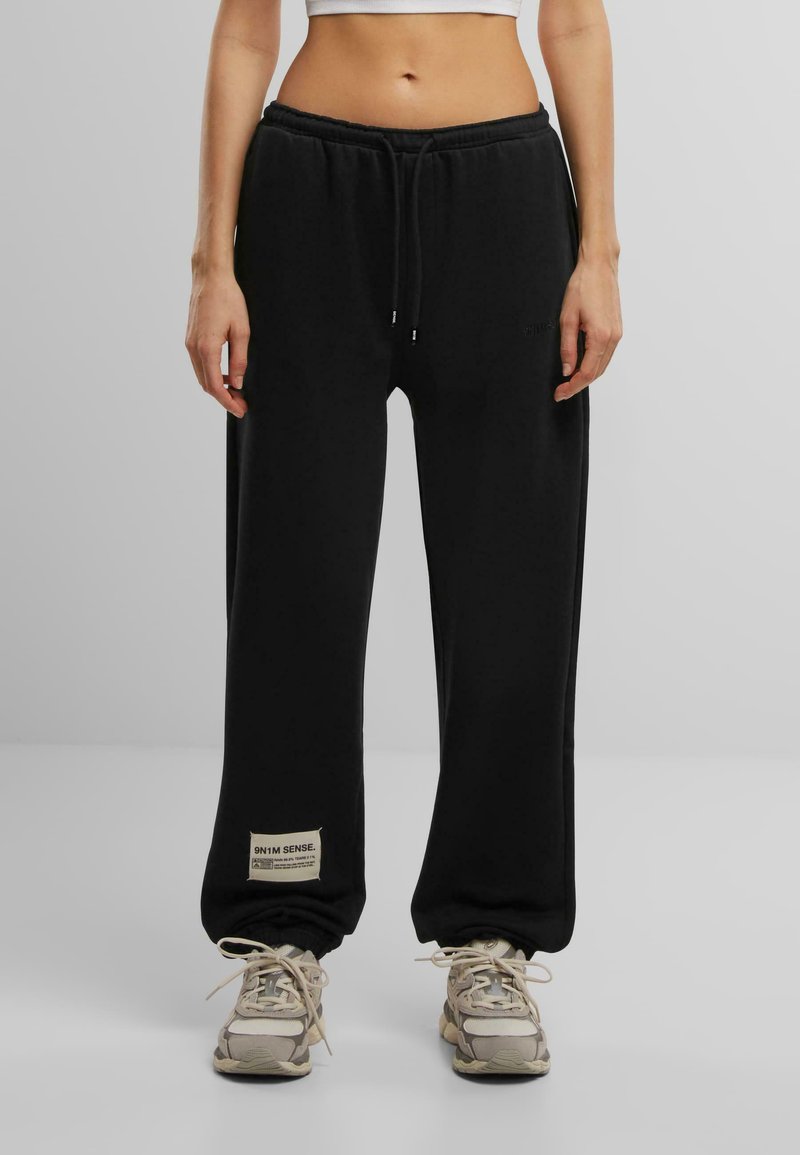 Schwarze Jogginghosen aus weichem Material, mit einem Kordelzug am Bund, elastischen Bündchen und einem kleinen Etikett mit Text am linken Bein.